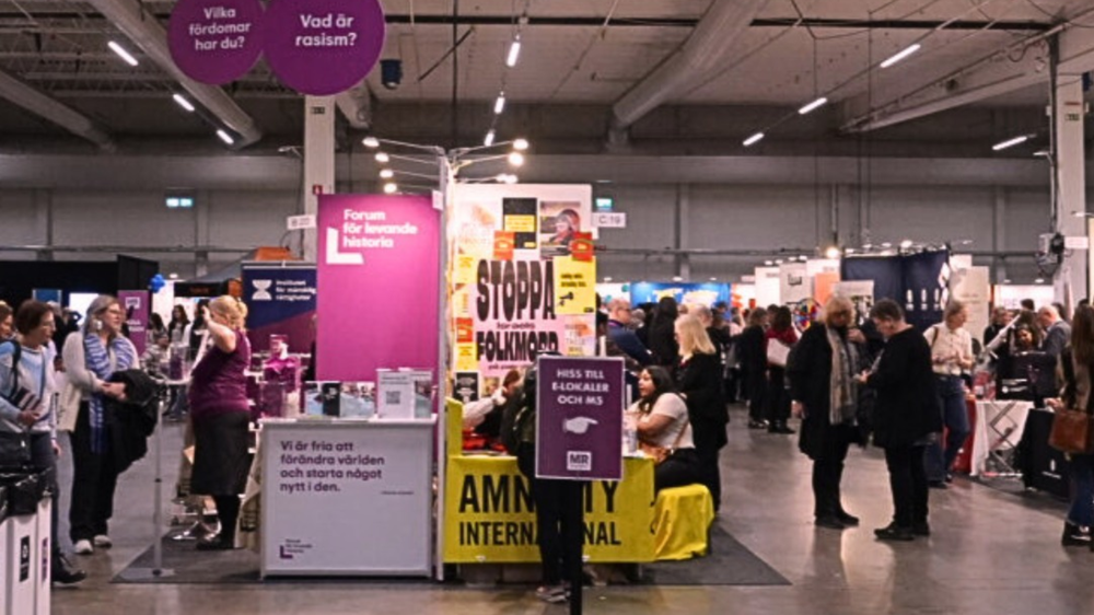 Mingel i en mässhall under MR-dagarna med informationsmontrar och besökare i samtal. I förgrunden syns Forum för levande historia och Amnesty International. Skyltar i taket ställer frågor som ”Vad är rasism?” och ”Vilka fördomar har du?”.