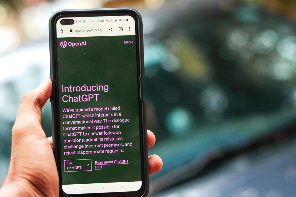 En hand håller upp en smartphone med information om ChatGPT.