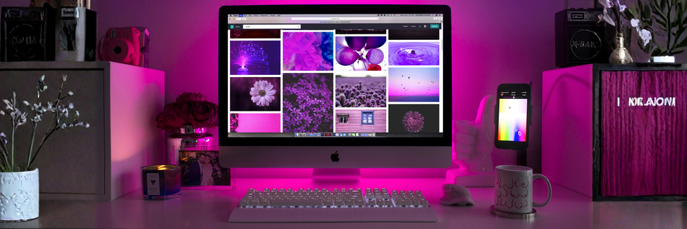 En datorskärm på ett skrivbord med massa bilder i klarrosa färger. Bakom datorn lyser ett rosa neonljus upp rummet.